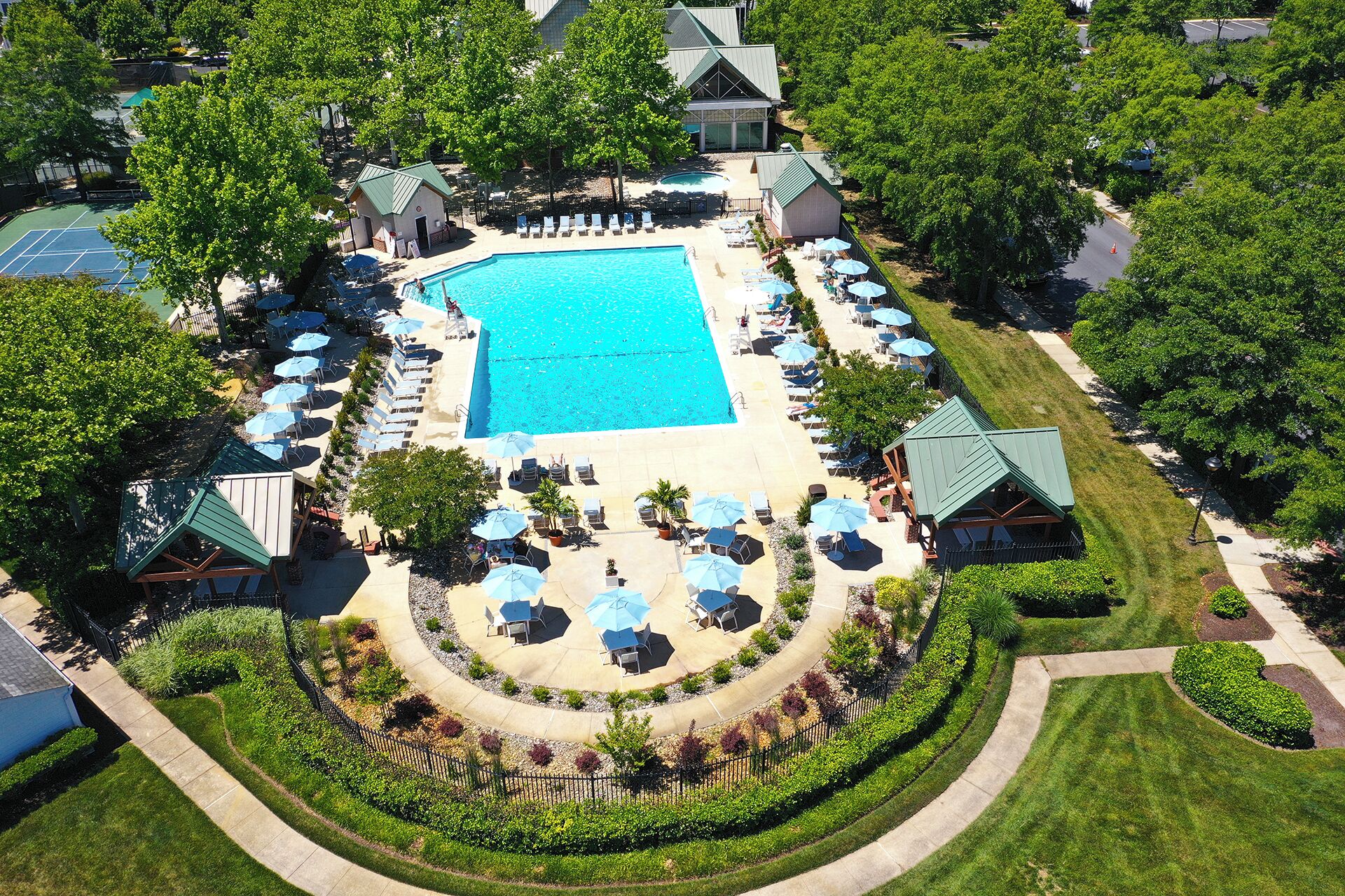 An aerial view of a resort with a central swimming pool surrounded by lounge areas and sun umbrellas.