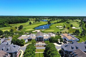 Un parcours de golf avec un étang, entouré d’immeubles résidentiels et sous un ciel bleu dégagé.