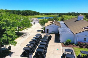Un campo de golf con un bar de aperitivos, una fila de carros de golf y un edificio con techo inclinado.