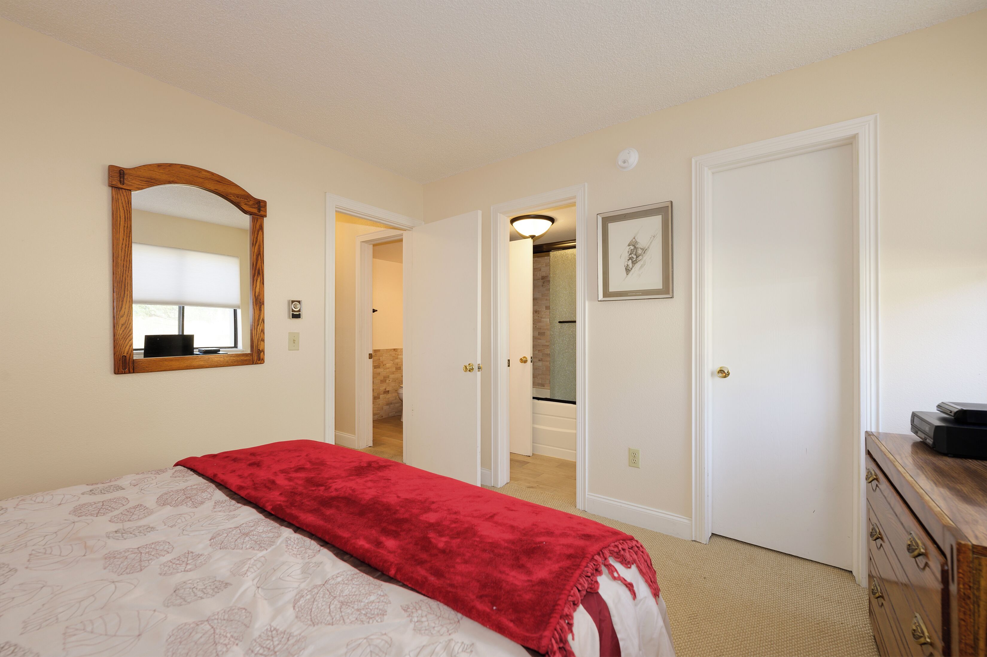 A bedroom with a bed, a mirror, a dresser, and a door leading to a bathroom.