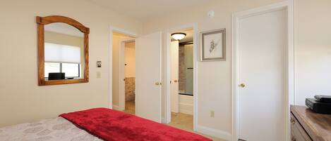 A bedroom with a bed, a mirror, a dresser, and a door leading to a bathroom.