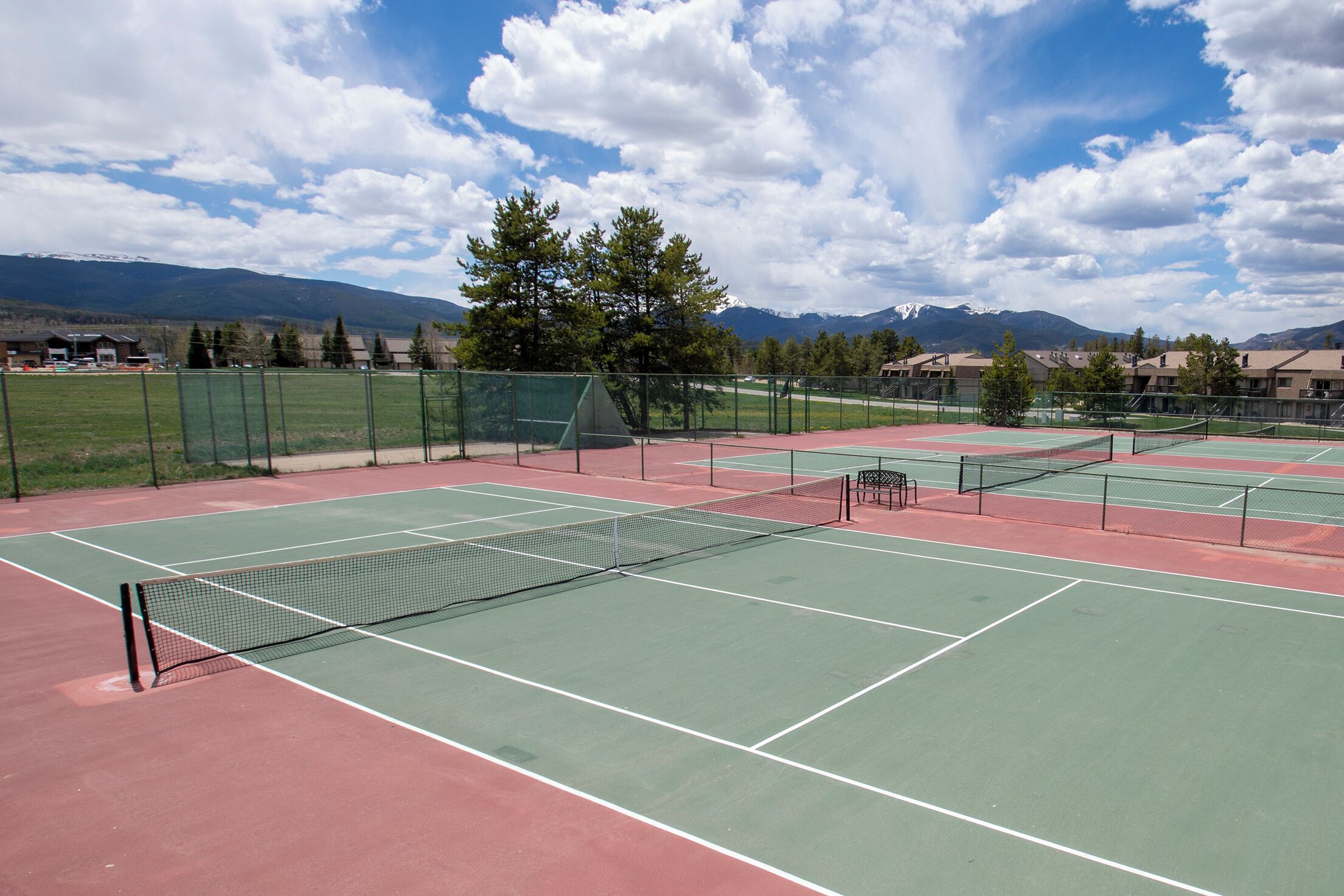 Ein Tennisplatz mit Netz, umgeben von einem Zaun, mit einem Bergpanorama im Hintergrund.