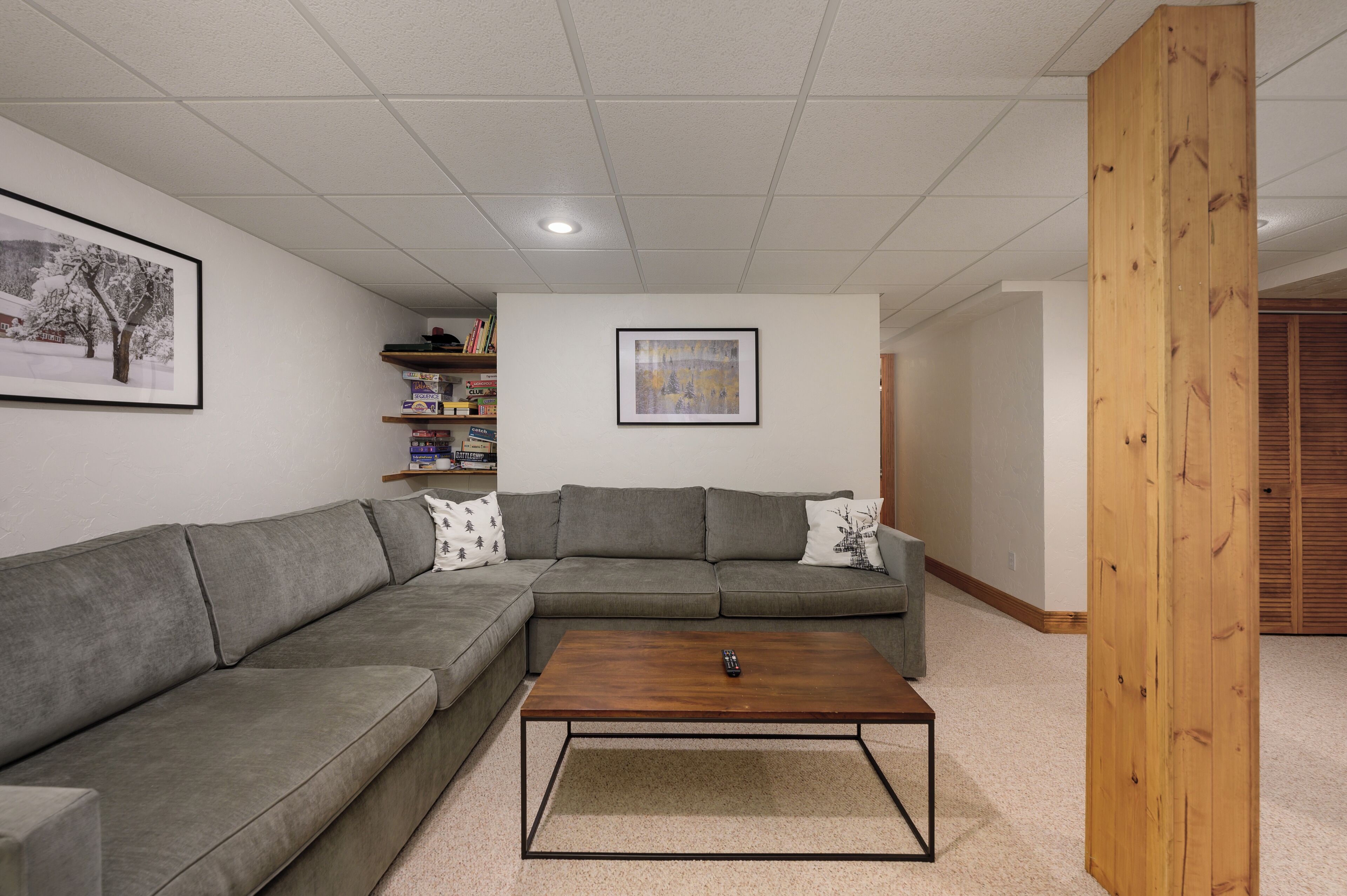 A living room with a gray sectional sofa, a wooden coffee table, and a bookshelf with books and decorative items.