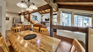 A spacious dining area with a wooden table and chairs, a chandelier, and large windows offering a view of the outdoors.