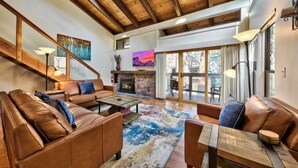 A spacious living room with a fireplace, leather sofas, a coffee table, and a large window with curtains.