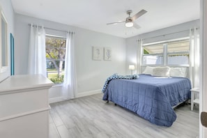 Une chambre à coucher avec un lit, un ventilateur de plafond et une fenêtre avec des rideaux.