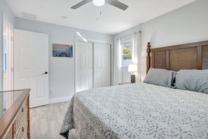 A bedroom with a bed, a ceiling fan, a nightstand with a lamp, and a window with curtains.
