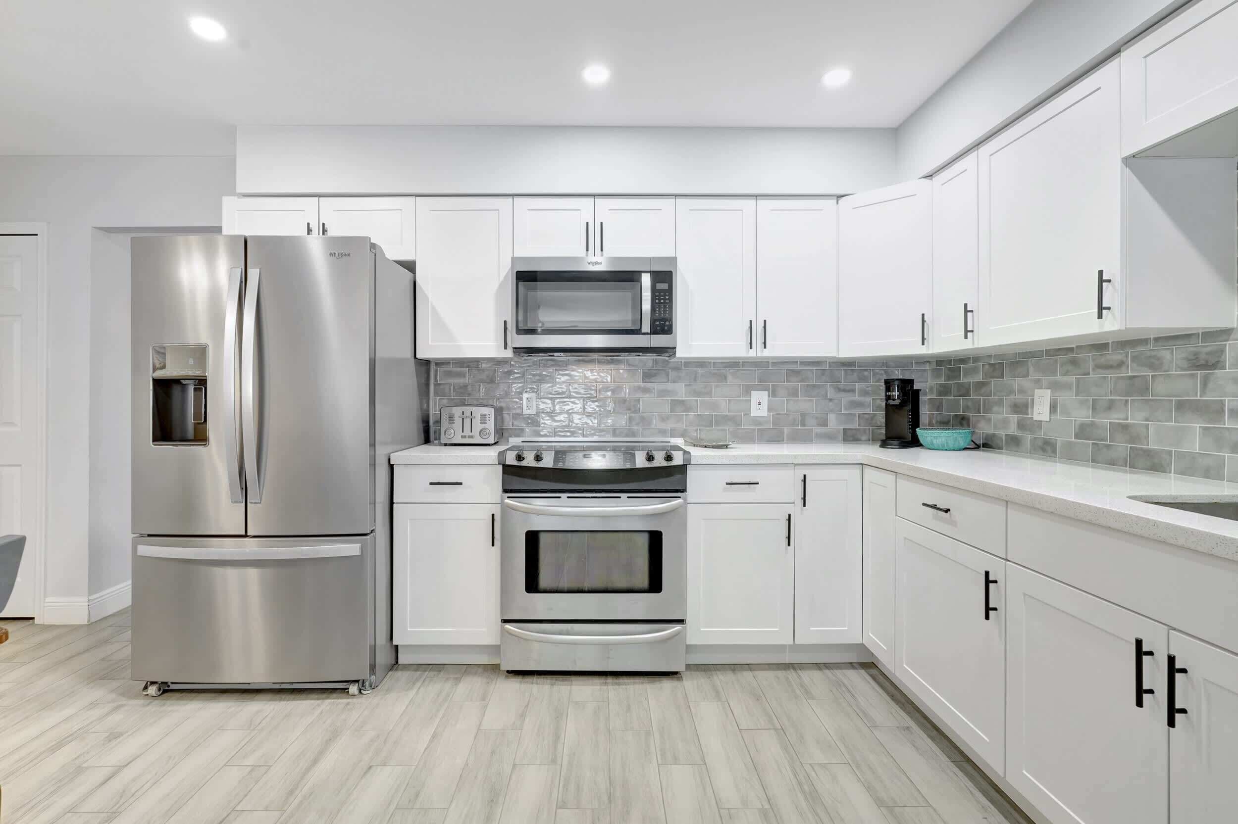 A modern kitchen with white cabinets, stainless steel appliances, and a grey tiled backsplash.