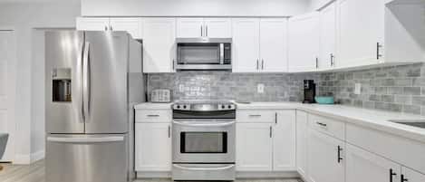 A modern kitchen with white cabinets, stainless steel appliances, and a grey tiled backsplash.
