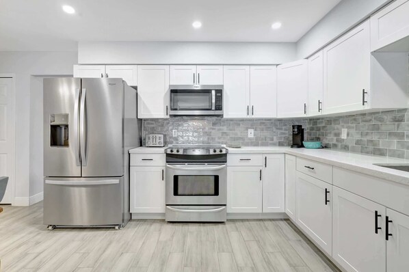 A modern kitchen with white cabinets, stainless steel appliances, and a grey tiled backsplash.