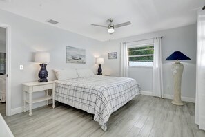 A bedroom with a bed, two bedside tables, a ceiling fan, a window with curtains, and a nightstand with a lamp.