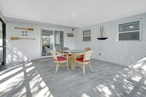 A room with a glass door leading to a patio, a round table with wicker chairs, and a sailboat decoration on the wall.