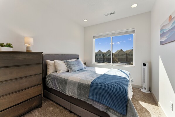 A bedroom with a bed, a dresser, a window with a view, and a standing heater.