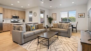 A modern living room with a sofa, coffee table, and a dining area with a table and chairs. - Hallser's Hive: 3 Bedroom, Pickleball Courts, Great Location! (Santa Clara)