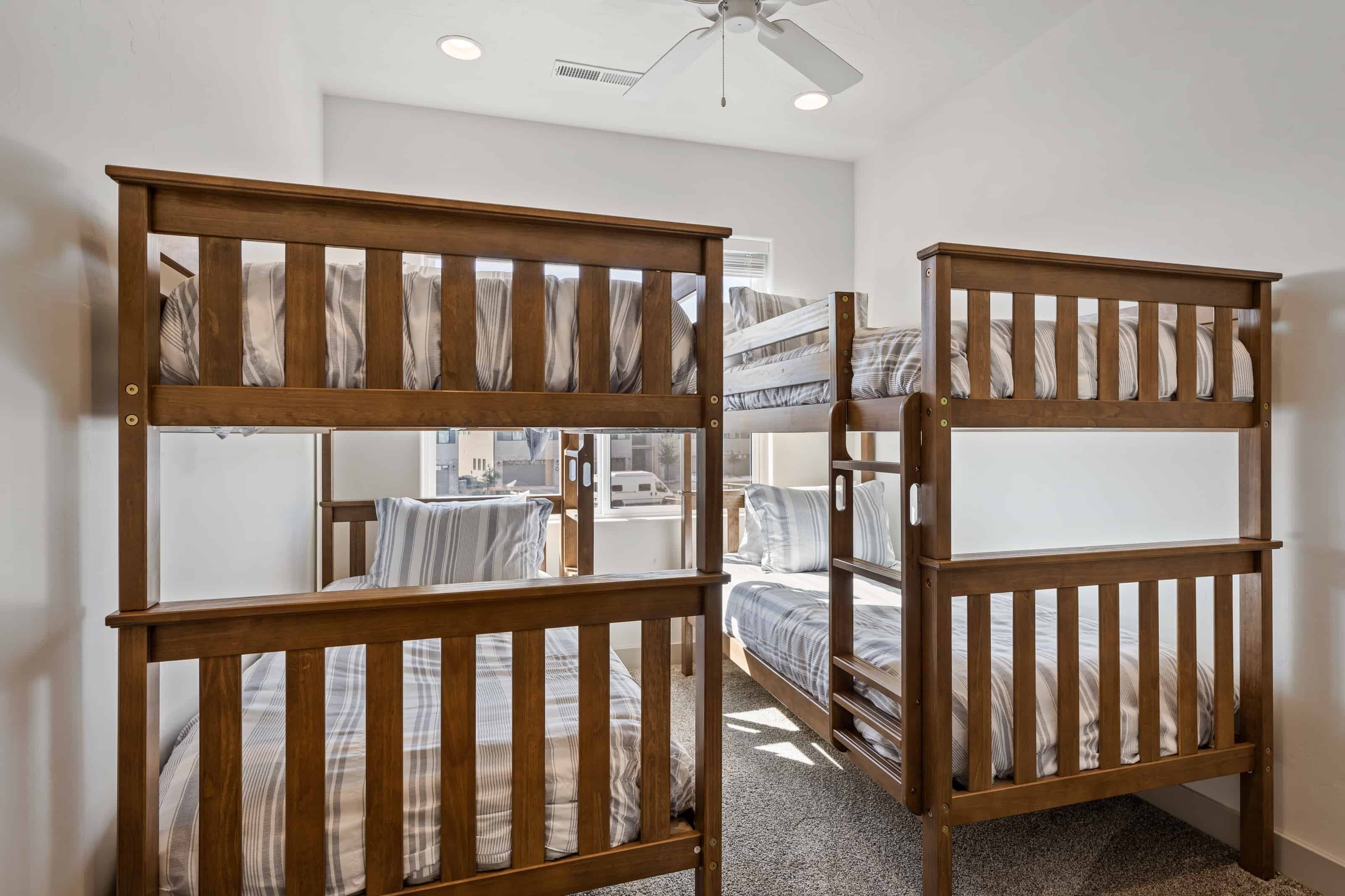 A room with two bunk beds, a ceiling fan, and a window with a view of a street.