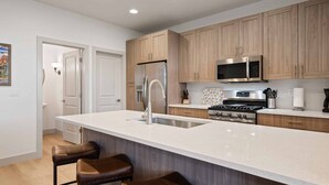 Une cuisine moderne avec des meubles en bois, des appareils en acier inoxydable, un grand îlot central avec des tabourets et un revêtement mural en carreaux.