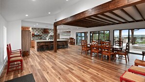 Un vaste espace de vie à aire ouverte doté d’un plancher en bois, d’une table à manger avec des chaises, d’un coin cuisine et de grandes fenêtres offrant une vue dégagée.
