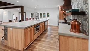 Une cuisine spacieuse avec des meubles en bois, un grand îlot central et une casserole en cuivre posée sur le plan de travail.