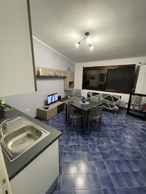 A compact kitchen with a built-in sink, a dining area with a table and chairs, a television, and a ceiling fan.