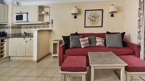 Un espacio habitable compacto con kitchenette, un sofá acolchado y una mesita.