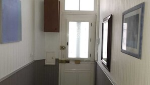 Un pasillo estrecho con una puerta al final, un banco y un cuadro en la pared.