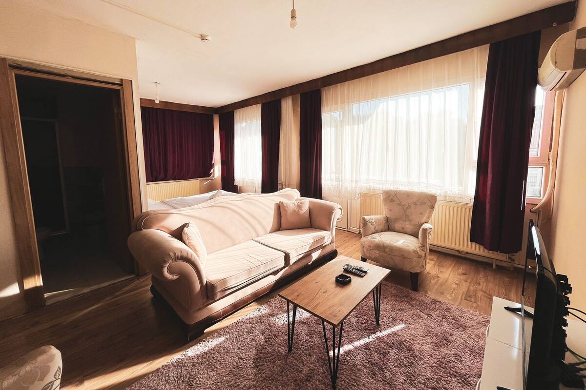 A spacious living room with a large sofa, a smaller armchair, a coffee table, and a television.