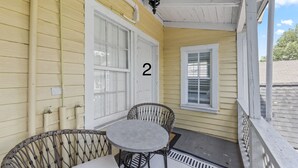 En veranda med ett bord och några stolar, en dörr med nummer 2 och ett fönster med persienner.