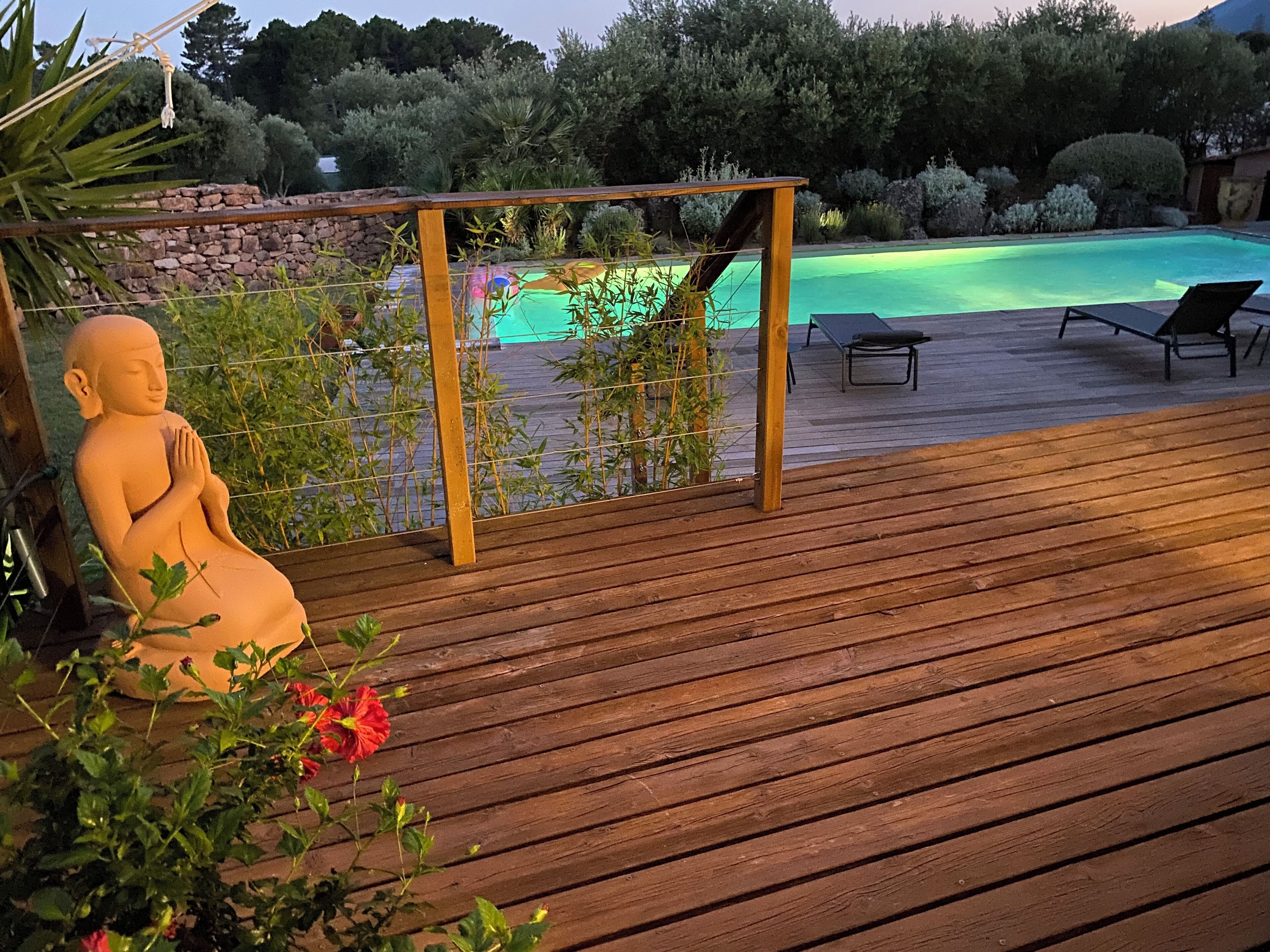 Een houten terras met een standbeeld, een zwembad en ligbedden.