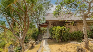 Una casa in pietra con un portico coperto, immersa nel verde e con un vialetto in pietra.