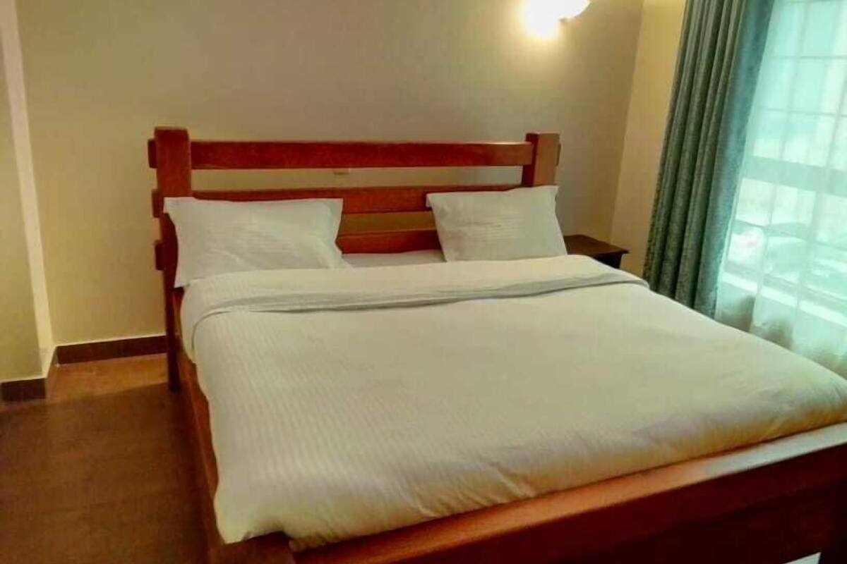 A neatly made bed with white linens in a room with wooden headboard and a nightstand.