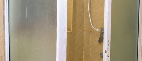 A small, enclosed shower area with a frosted glass door and a showerhead mounted on the wall.