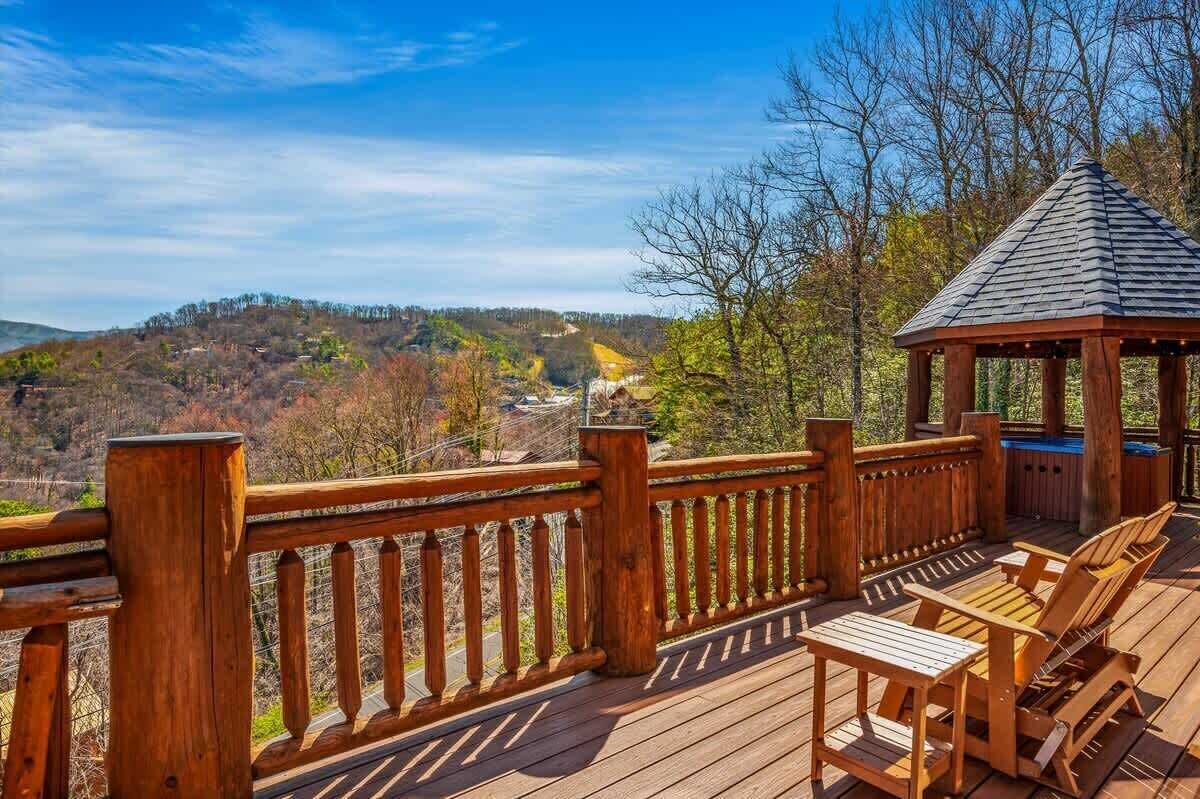 Una terraza de madera con un mirador, mobiliario exterior y una vista panorámica de colinas.