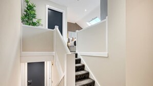 A staircase with a dark carpeted finish, white walls, and a small plant on the landing. - Host & Stay | Halifax House Living (Liverpool)