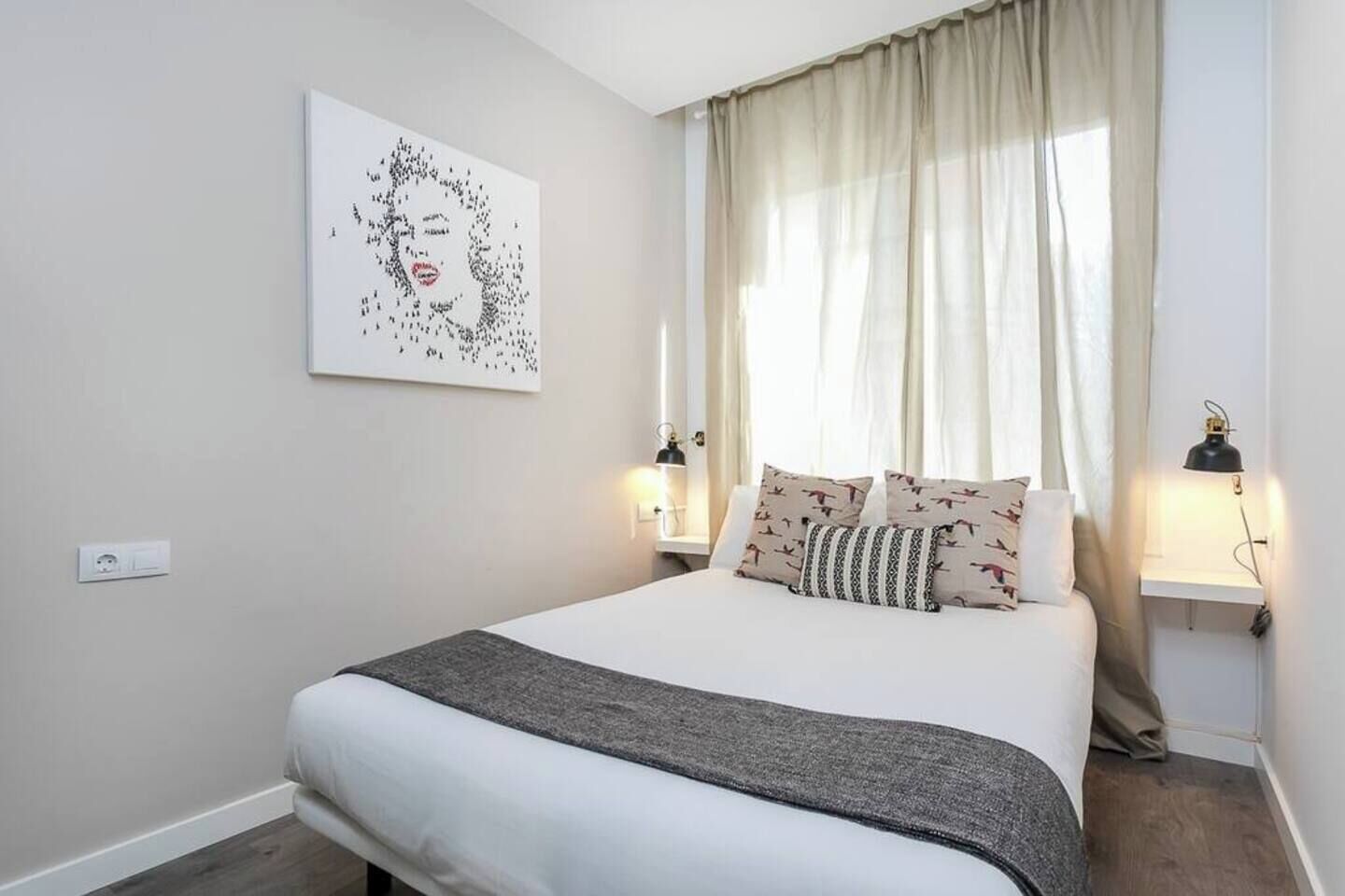 Een keurig opgemaakte slaapkamer met een groot bed, een kunstwerk aan de muur en twee bedlampen.