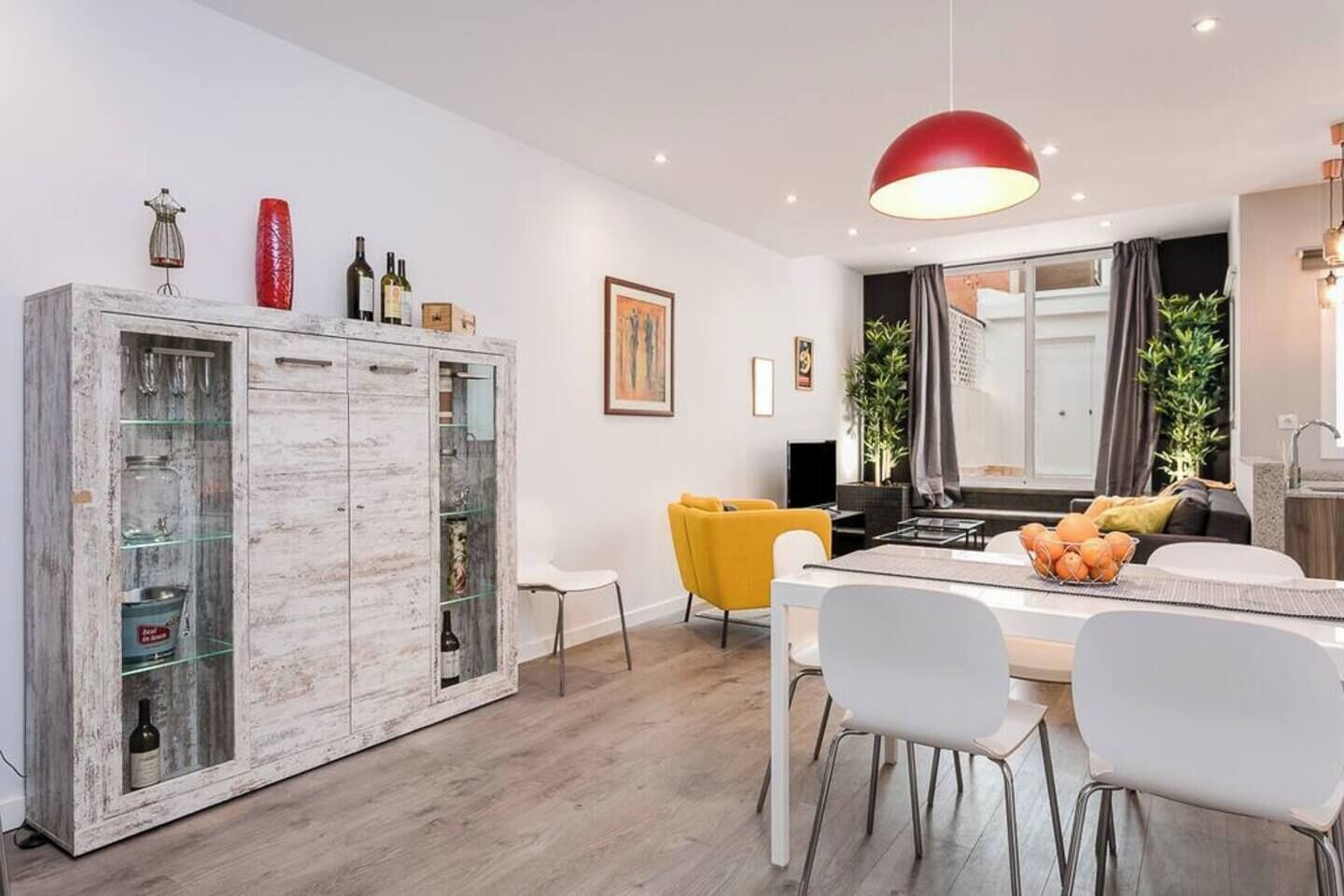 Une cuisine moderne avec un coin repas, un grand meuble avec des portes en verre et un luminaire suspendu rouge.