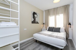 Une chambre à coucher comprenant un lit, une table de chevet, une lampe, une fenêtre avec des rideaux et une œuvre d’art accrochée au mur.
