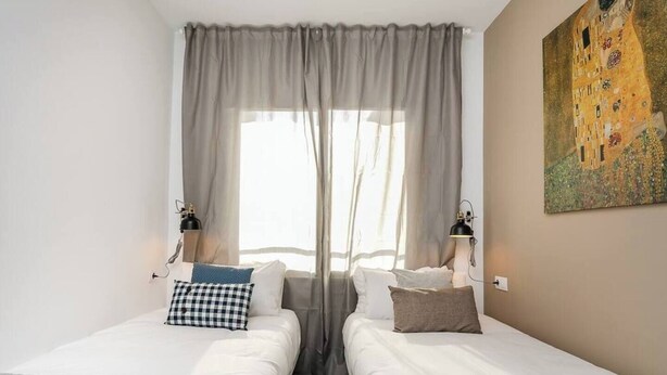 Hotelkamer met twee bedden, een groot raam met dunne gordijnen, twee wandlampen en een schilderij aan de muur.