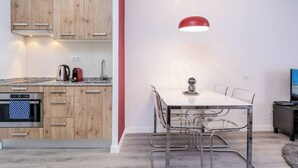 Een moderne keuken met houten kastjes, een inbouwoven en een eethoek met een witte tafel en metalen stoelen.