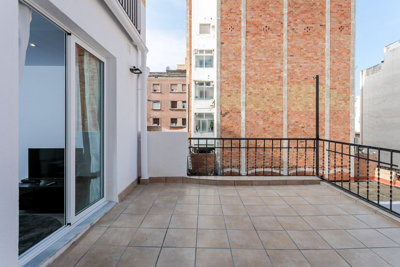 A balcony with tiled flooring, a black metal railing, and a view of adjacent buildings.