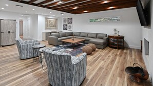 Ein modernes Wohnzimmer mit einem Ecksofa, zwei Sesseln, einem Couchtisch und einem an der Wand befestigten Fernseher.