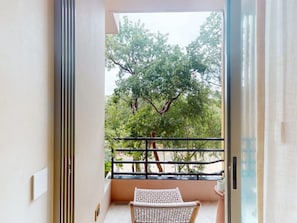 Enjoy the serene view from this balcony overlooking a tree-lined area, featuring a comfortable chair and metal railing.