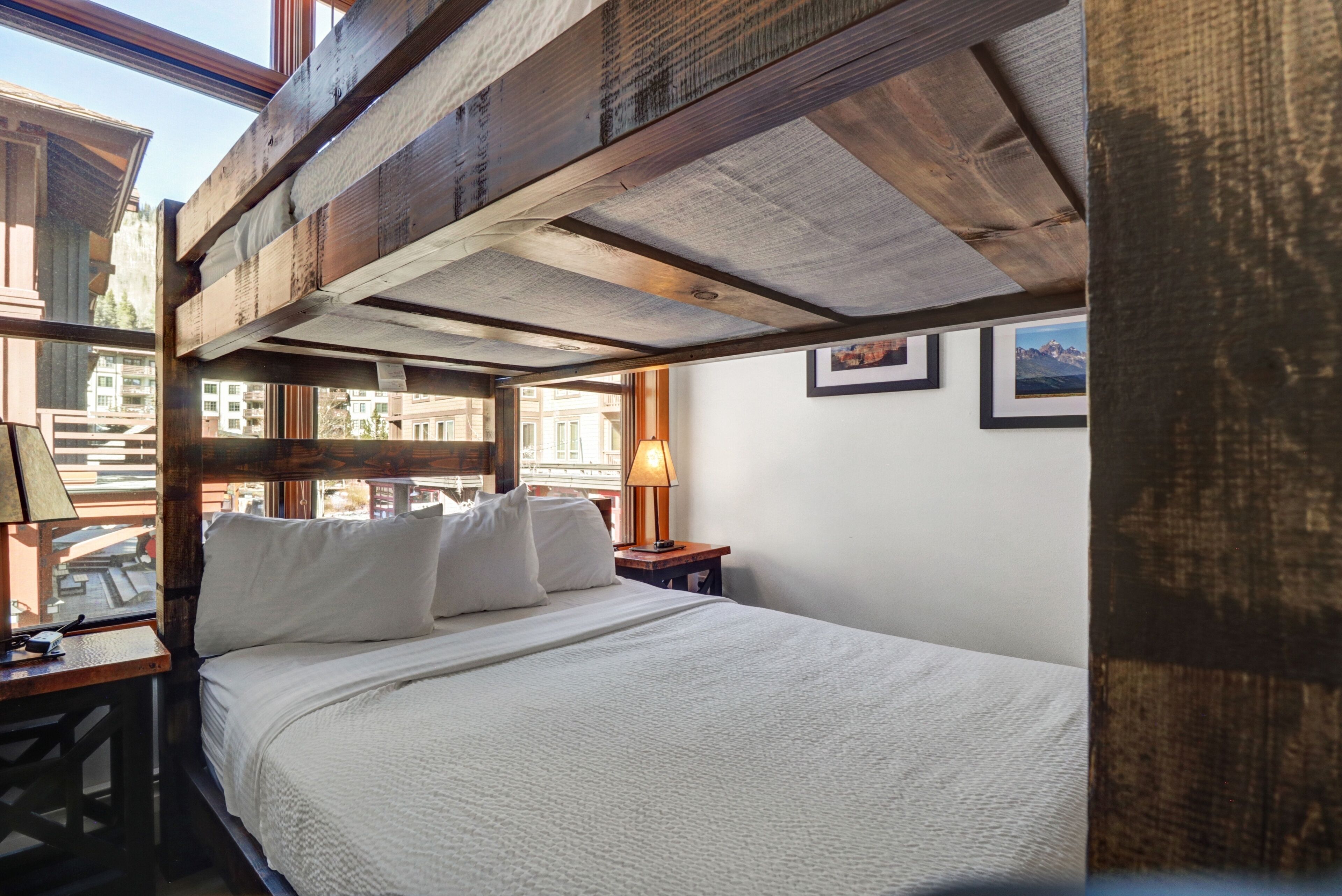 A bedroom with a wooden ceiling, a bed with white bedding, a nightstand with a lamp, and framed pictures on the wall.