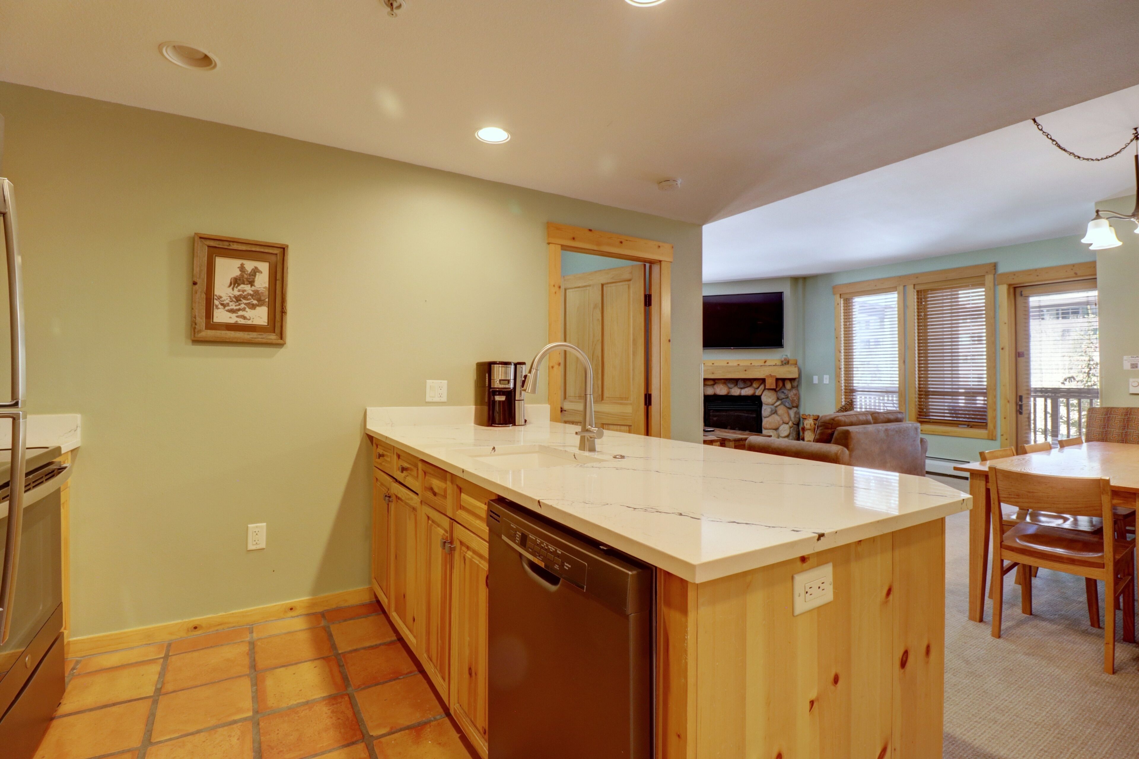 A kitchen with a dishwasher, wooden cabinets, a white countertop, and a dining area with a table and chairs.