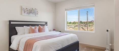 A bedroom with a bed, a ceiling fan, a window with a view, and a wall-mounted heater.