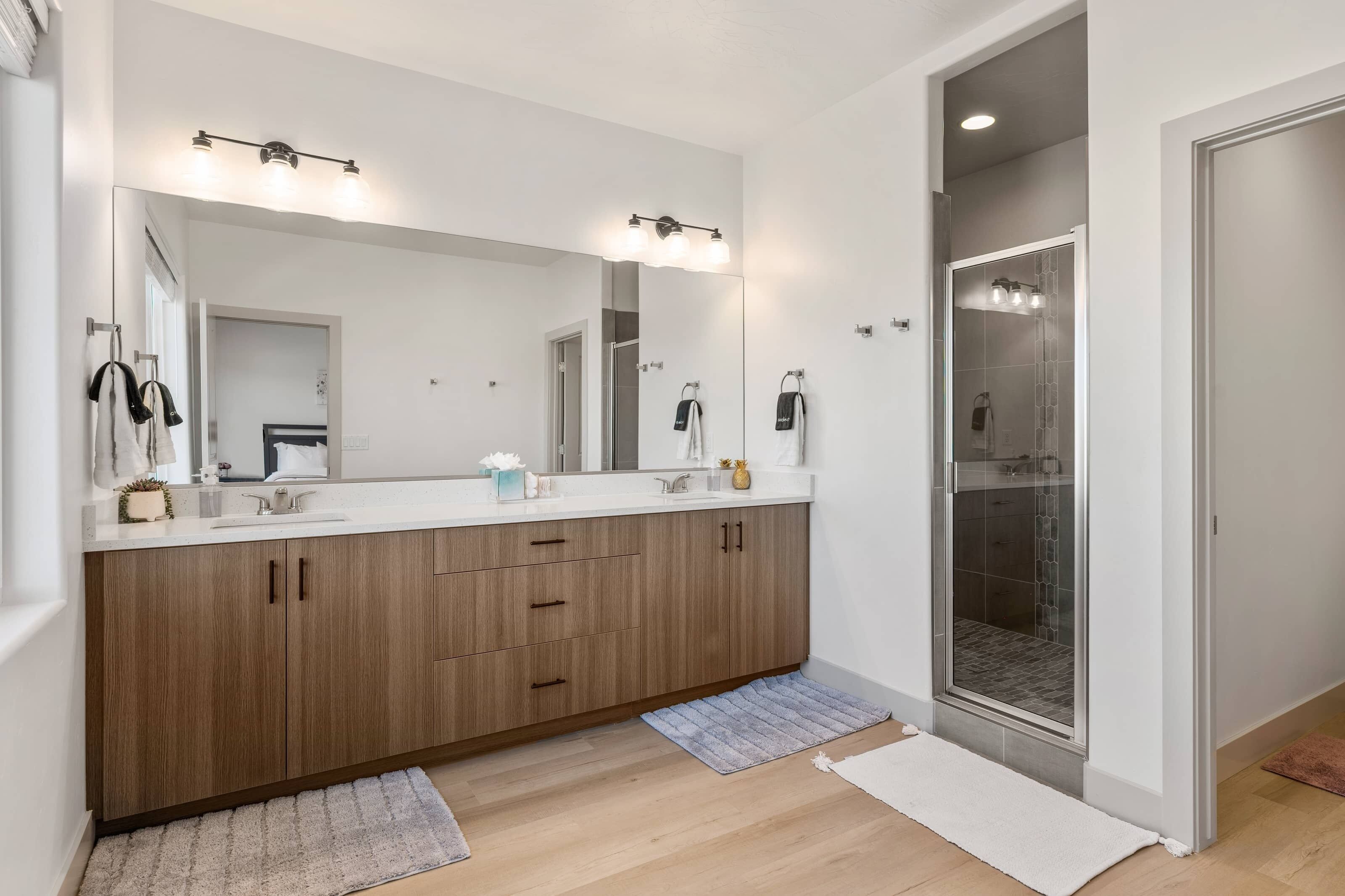 Ein modernes Badezimmer mit großem Spiegel, zwei Waschbecken und einer Duschkabine aus Glas.