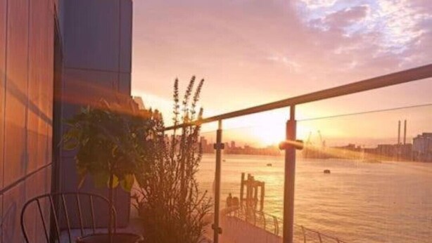 A balcony with a table and chairs, overlooking a river with a sunset. - Snuggle Inn - Riverside apartment- Woolwich Ferry, Mins to O2 Arena (Woolwich)
