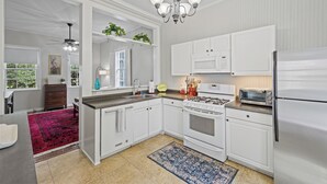 Una cucina moderna con mobili bianchi, piano cottura a gas, forno a microonde e frigorifero. Sul pavimento è presente un tappeto rosso e sopra la cucina un ventilatore a soffitto.
