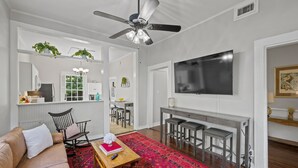 Un soggiorno moderno con ventilatore a soffitto, una televisione grande, un'area pranzo con sgabelli da bar e un tappeto rosso decorato.