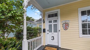 Una casa con un portico bianco, una porta con il numero 3 e uno stemma apposto al muro.