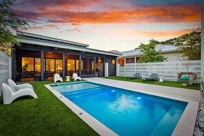 Una casa moderna con piscina, patio coperto e prato curato.